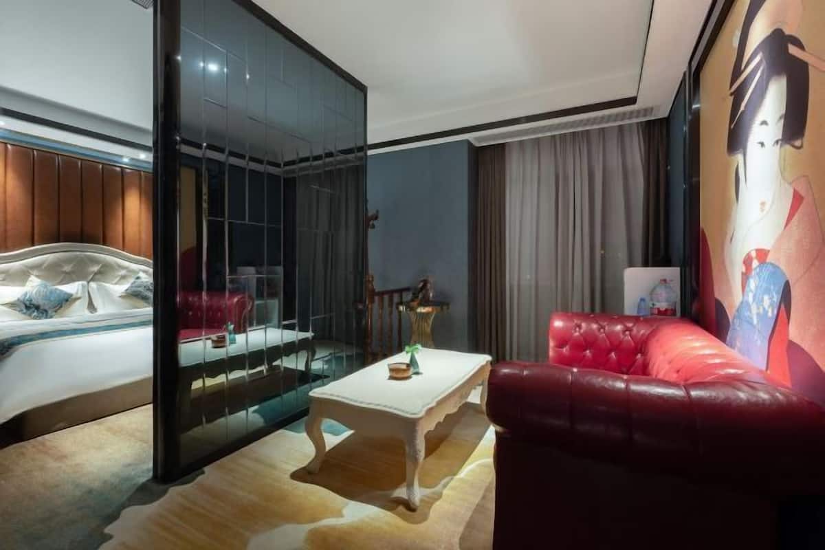 Une chambre d’hôtel avec un lit, un canapé en cuir rouge, une cloison en verre et un tableau au mur.