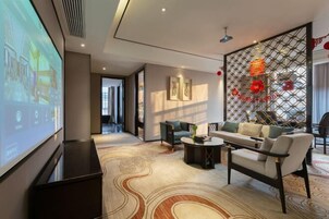 Quarto de hotel moderno com uma tela grande, um sofá, uma mesa de centro e um painel decorativo com flores vermelhas.