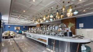 Eine moderne Hotelhalle mit einer gebogenen Rezeption, verschiedenen Sitzbereichen und Pendelleuchten.