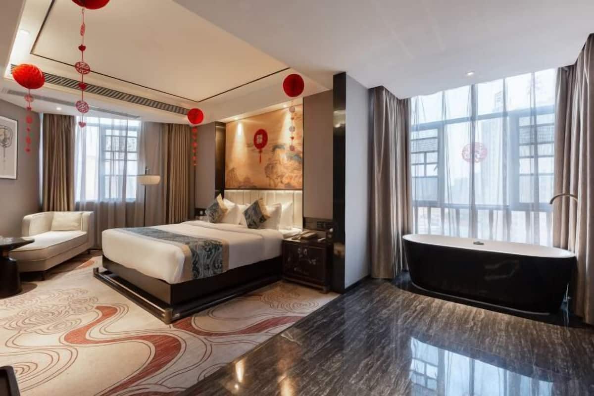 Une chambre d’hôtel moderne dotée d’un grand lit, d’un coin salon, d’une baignoire et d’une grande fenêtre.