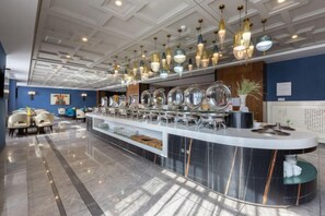 Un hall d’hôtel moderne doté d’un comptoir d’accueil central, de plusieurs espaces de détente et d’un plafond décoratif.