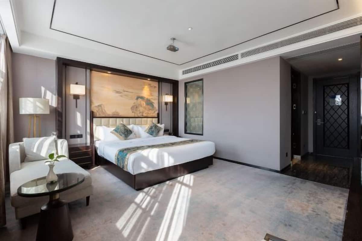 Une chambre d’hôtel moderne, dotée d’un grand lit, d’un coin salon avec une table en verre et d’un tableau au mur.