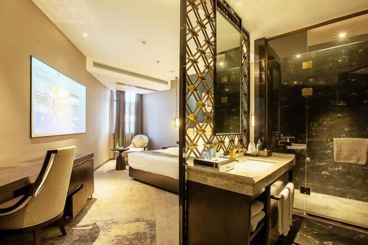 Une chambre d’hôtel équipée d’un lit, d’un bureau, d’un grand miroir, d’une douche et d’un téléviseur fixé au mur.