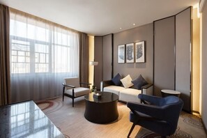 Una habitación de hotel moderna con un sofá, dos sillones, una mesa de centro y una mesita auxiliar.
