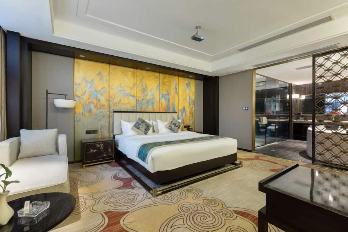 A modern hotel room with a large bed, a sofa, a small table, and a decorative wall.