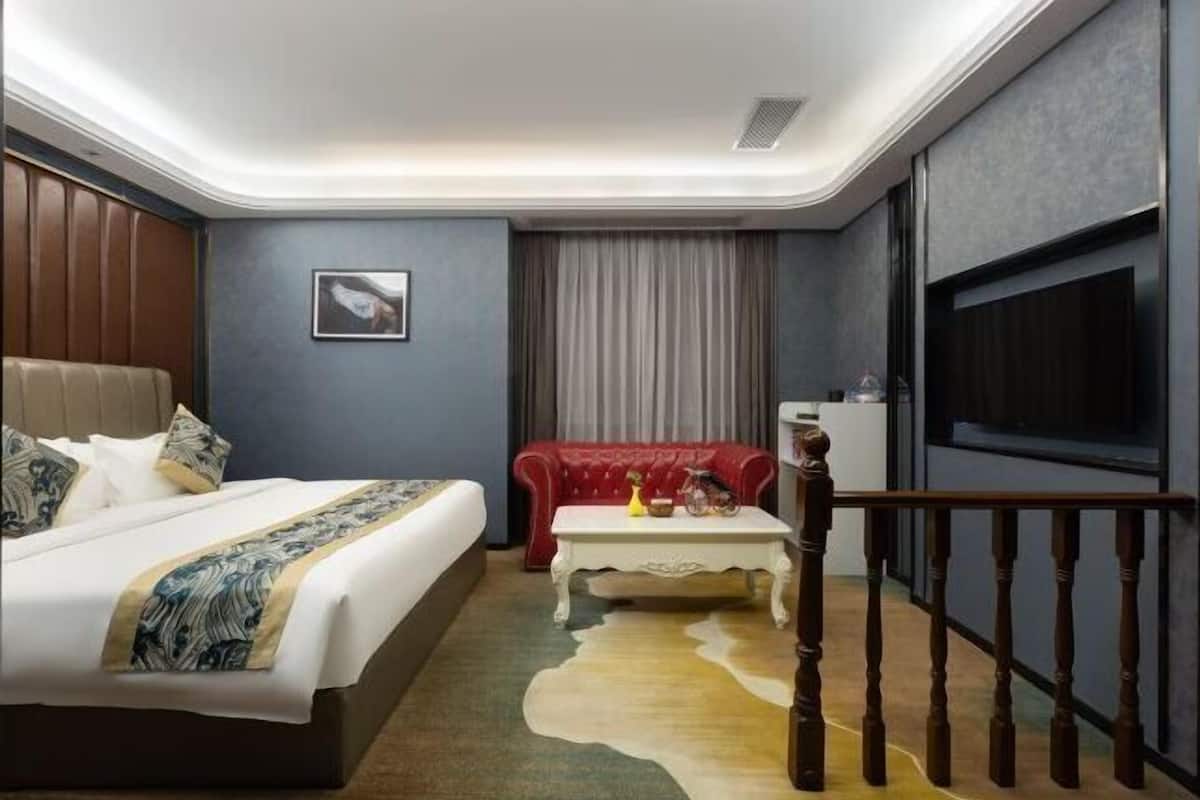 A hotel room with a large bed, a red sofa, a small table, and a TV.