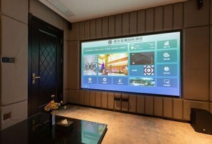 Ein Hotelzimmer mit einem großen Bildschirm, der eine digitale Benutzeroberfläche zeigt, einer Tür und einem kleinen Tisch mit Blumen in einer Vase.