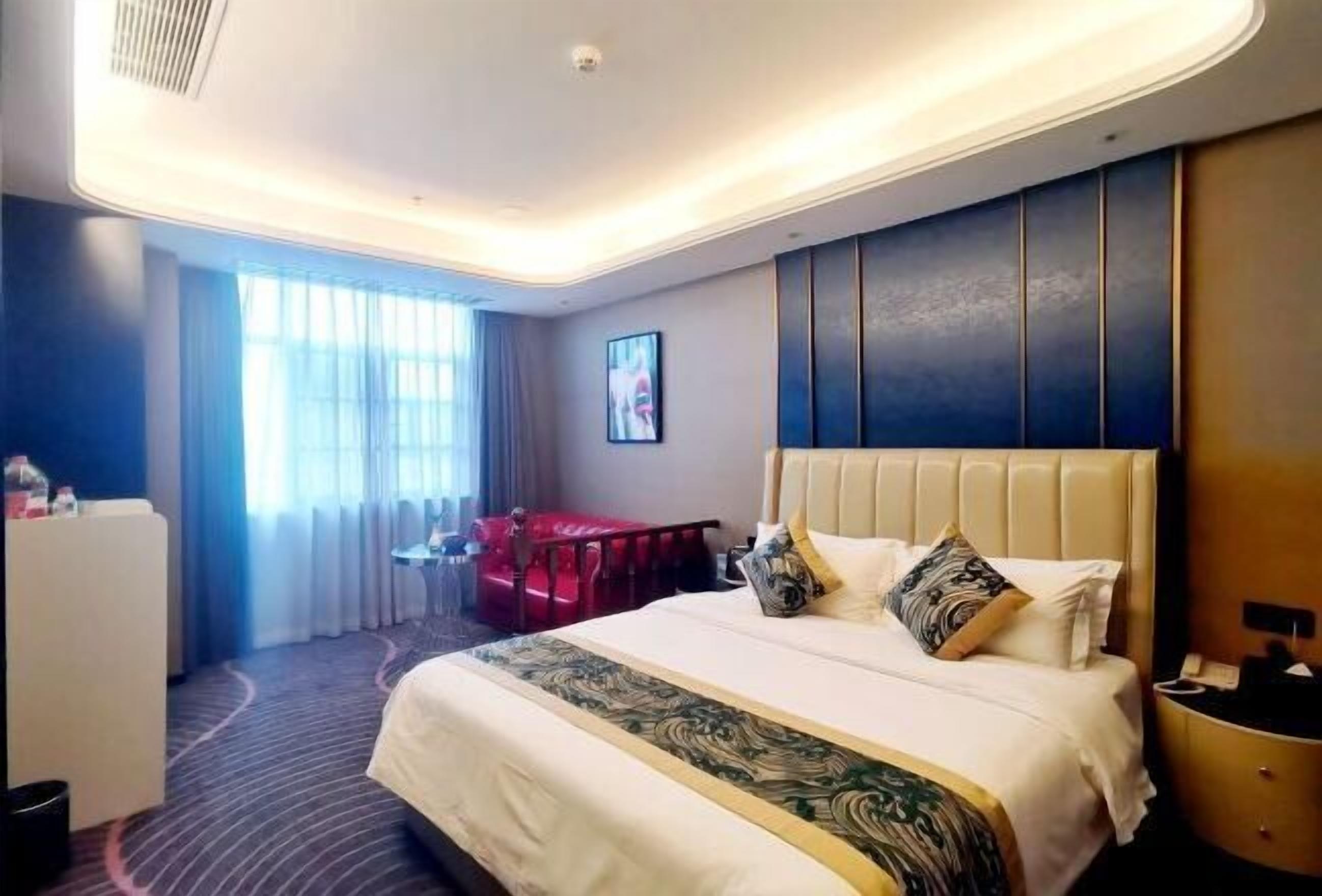 A hotel room with a large bed, a desk, a chair, and a window with curtains.
