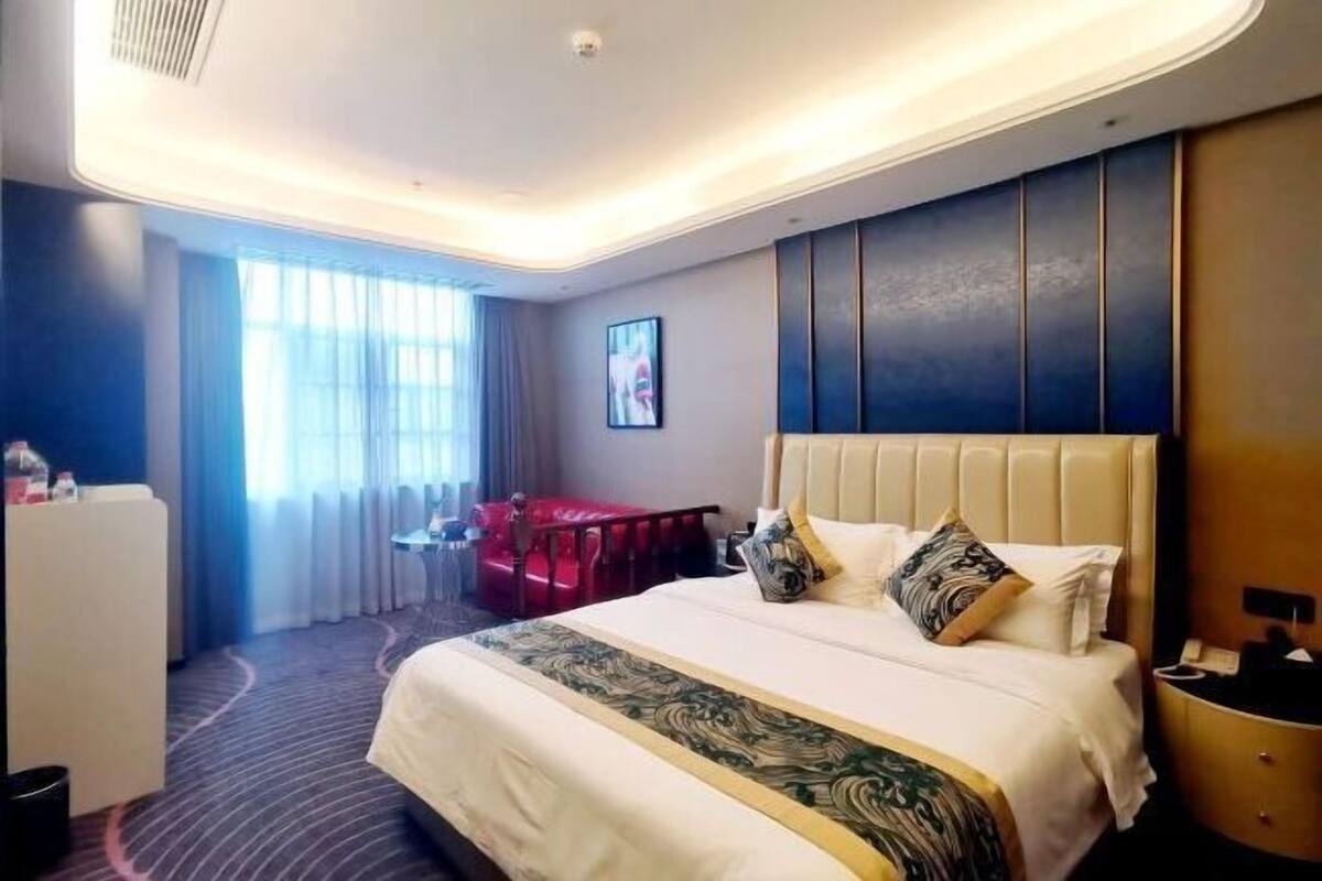 A hotel room with a large bed, a desk, a chair, and a window with curtains.