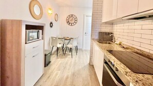 Eine moderne Küche mit weißen Schränken, einer Granit-Arbeitsplatte und einem eingebauten Backofen. Es gibt einen Essbereich mit Tisch und Stühlen sowie eine Wanduhr.