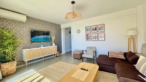 Ein modernes Wohnzimmer mit einer Wand im Steinoptik, einem Flachbildfernseher, einem Couchtisch aus Holz, einem braunen Sofa und einer Stehlampe.