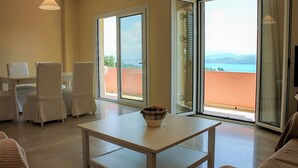 Una habitación con una mesa de comedor y sillas, un sofá blanco, y vistas al mar a través de grandes puertas correderas de cristal.