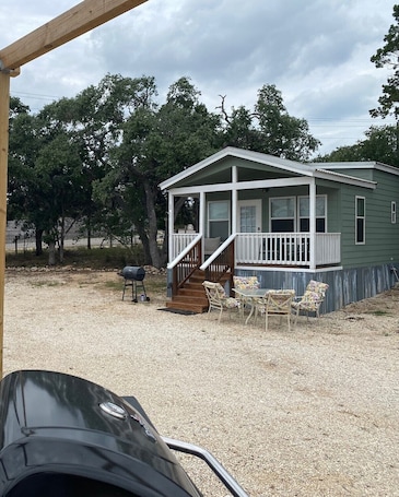 A small, single-story house with a porch, a barbecue grill, and outdoor seating.