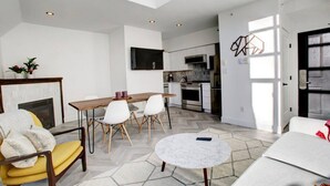 Een moderne woonkamer met een open haard, een eethoek met een houten tafel en stoelen, een keuken met een kookplaat en oven, en een groot raam dat zorgt voor daglicht.