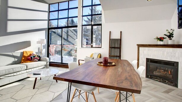 Een moderne woonkamer met een grote houten eettafel, een open haard en grote ramen met uitzicht op de omgeving.