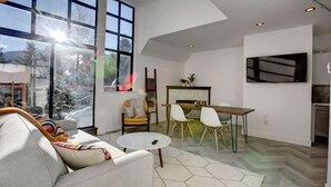 Een moderne woonkamer met een groot raam, een bank, een ronde salontafel, en een eethoek met stoelen en een tafel.
