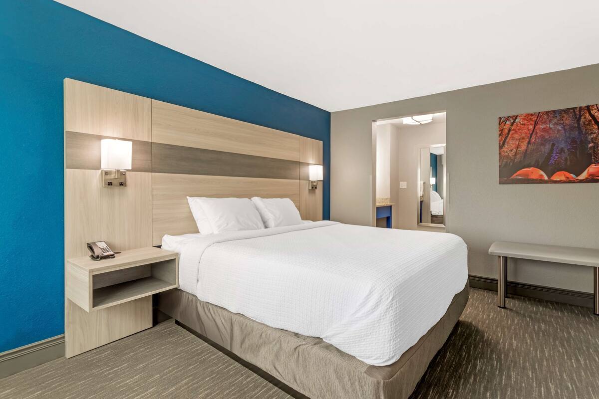 A hotel room with a large bed, bedside tables, a desk, and a painting on the wall.
