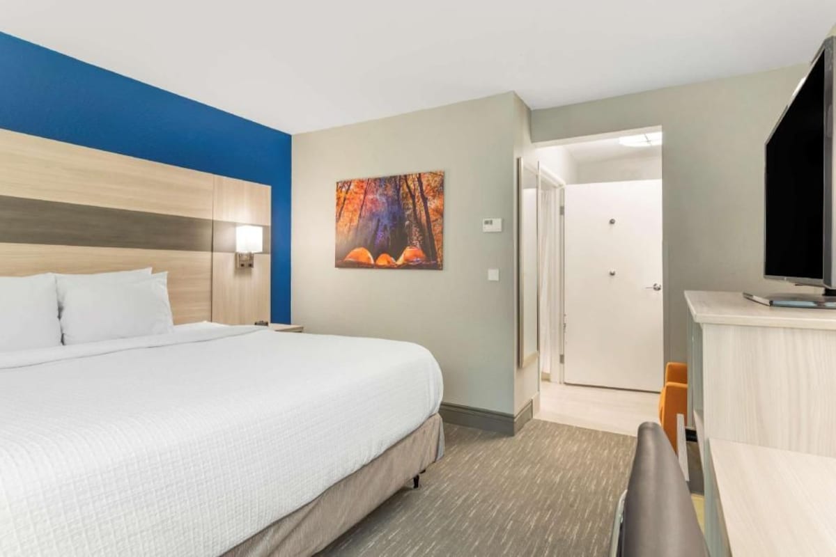 A hotel room with a bed, a desk, a chair, a TV, and a painting on the wall.