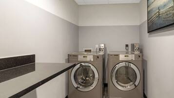 A laundry room with two front-loading washing machines, a dryer, and a wall-mounted television.