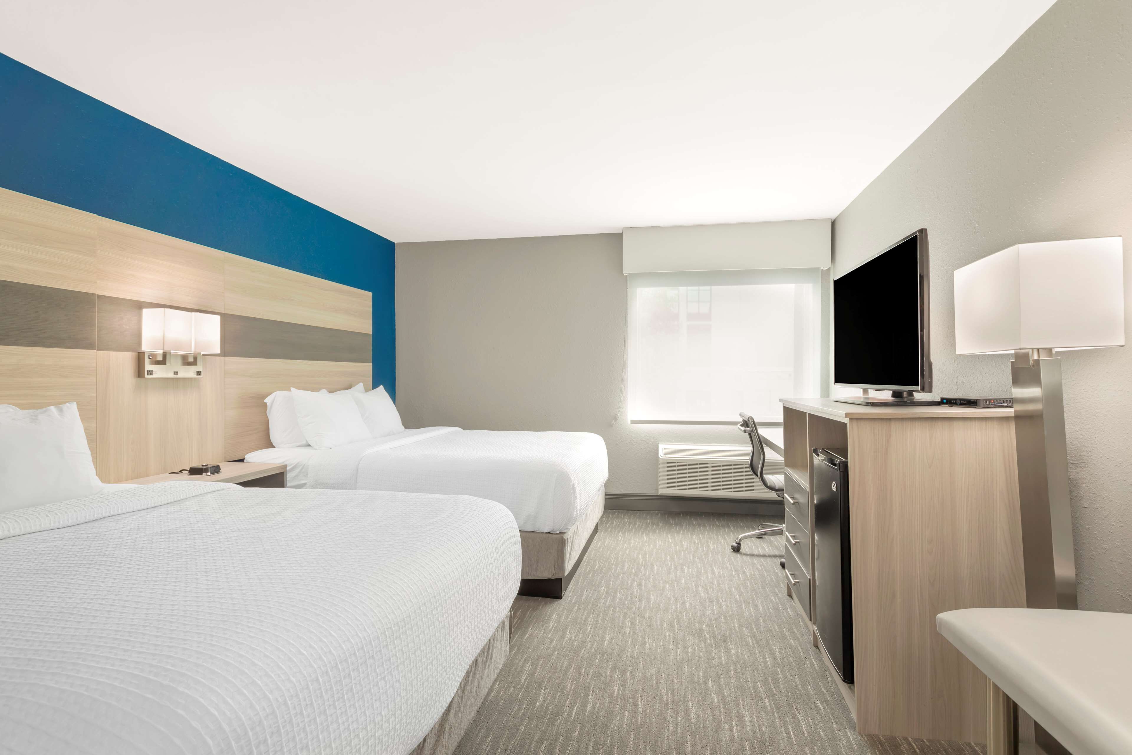 Una habitación de hotel con dos camas, un escritorio, un televisor y un minibar.