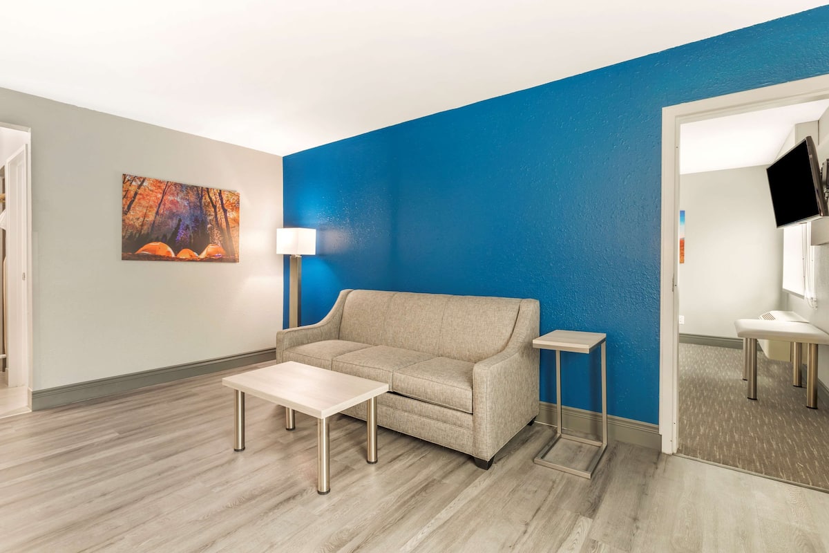 A modern hotel room with a beige sofa, a small table, a lamp, and a painting on the wall.