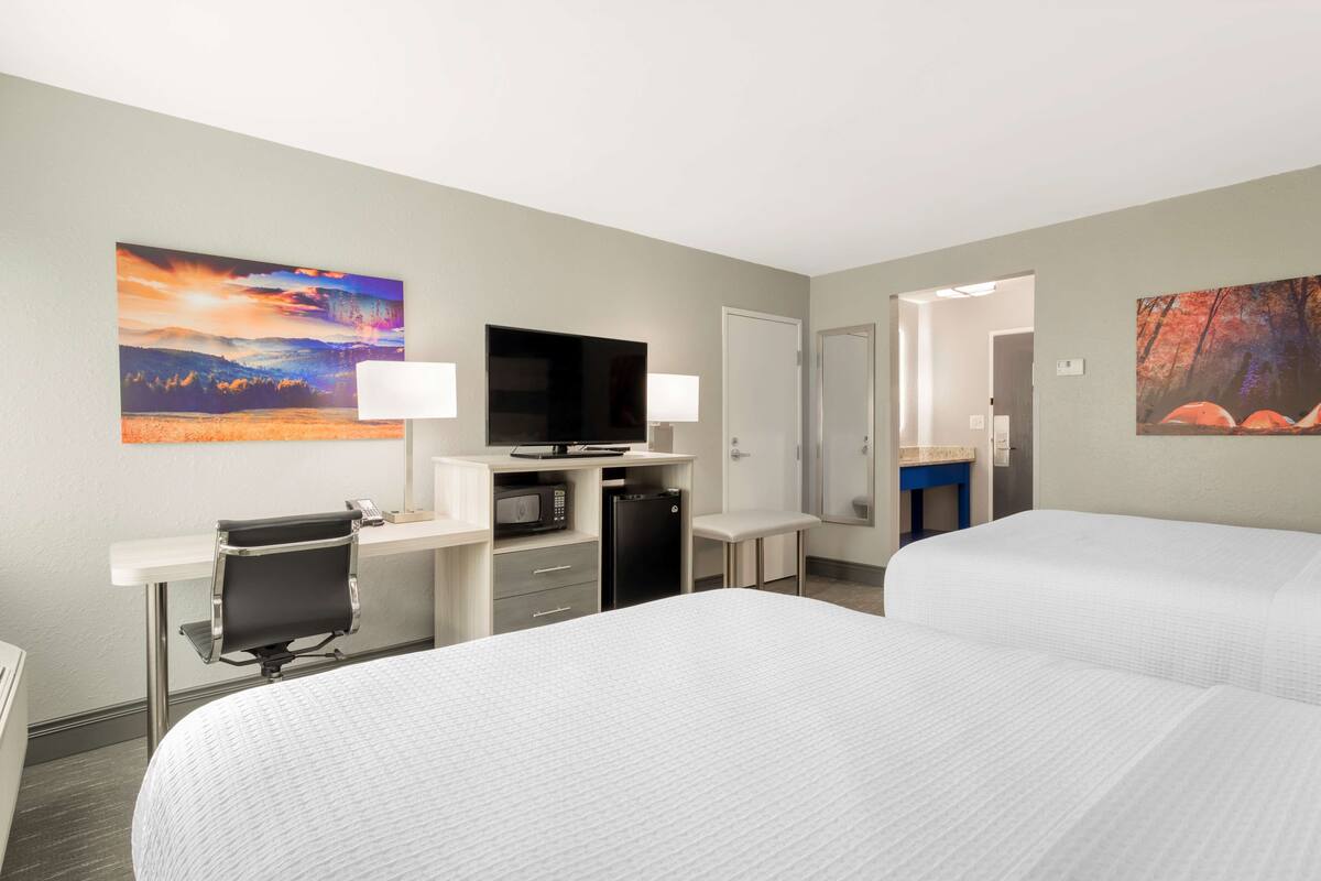 A hotel room with two beds, a desk with a computer, a TV, and a microwave.