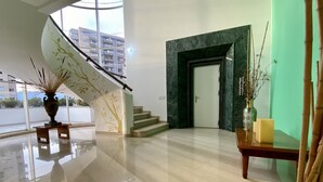Un interior moderno con una escalera, un florero con ramas y una pared verde.