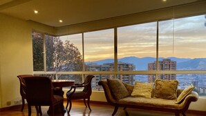 Amplia habitación con un gran ventanal que ofrece vistas a la ciudad, suelo de madera y un sofá con cojines.