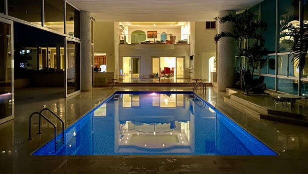 Una piscina interior moderna con cerramiento de vidrio, un balcón en el segundo piso y un interior bien iluminado.