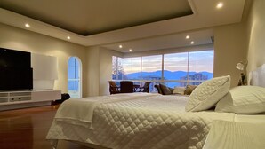 Un dormitorio moderno con una cama grande, un televisor y vistas de la ciudad a través de amplios ventanales.