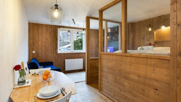 Una habitación acogedora con detalles de madera, una mesa de comedor lista con platos y vasos, y vistas al exterior a través de una ventana.