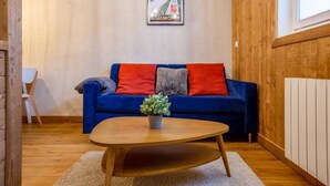 Una sala de estar acogedora con un sofá azul, cojines rojos y grises, una mesa de centro de madera y un cuadro en la pared.