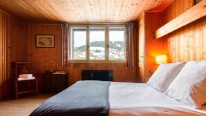 A wooden room with a bed, a window with a view of a snowy landscape, and a lamp on the right.