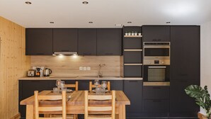 A modern kitchen with dark cabinetry, a wooden dining table, and built-in appliances.