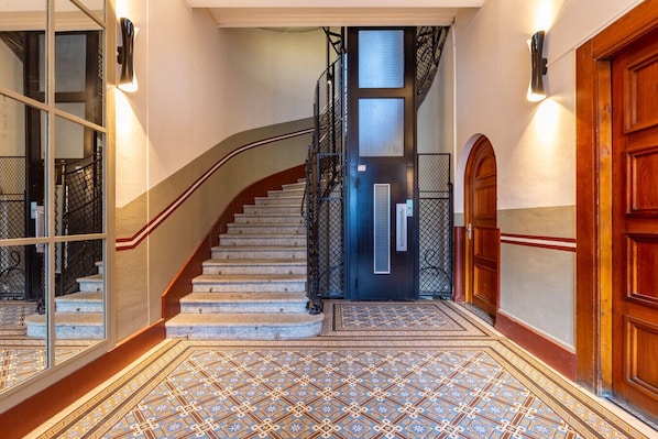 A grand staircase with a black metal railing, a wooden door, and a patterned floor.