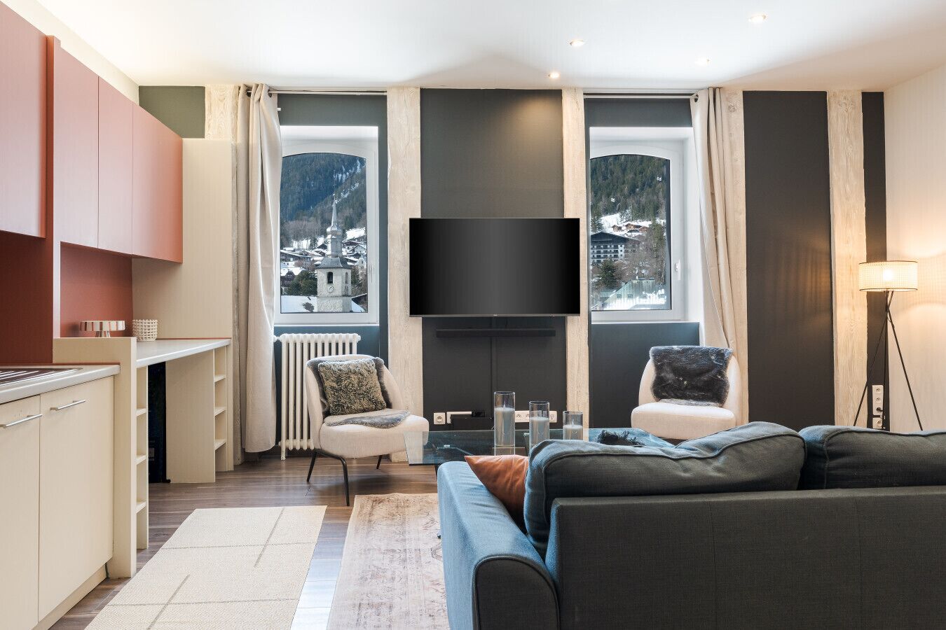 Een moderne woonkamer met een bank, twee fauteuils, een flatscreen televisie en grote ramen met uitzicht op bergen.