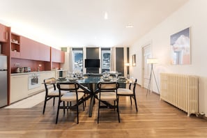 A modern kitchen with a dining area, wooden flooring, and a large window.