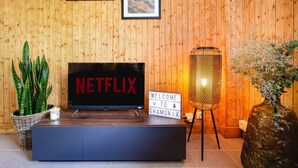 Un mur en bois orné de tableaux encadrés, un panneau Netflix, une pancarte de bienvenue, une plante et une lampe.