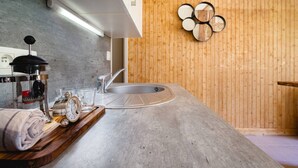 Une cuisine moderne avec un plan de travail en béton, un évier encastré et un mur en bois agrémenté d’un miroir décoratif.