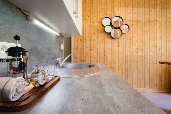 Une cuisine moderne avec un plan de travail en béton, un évier encastré et un mur en bois agrémenté d’un miroir décoratif.