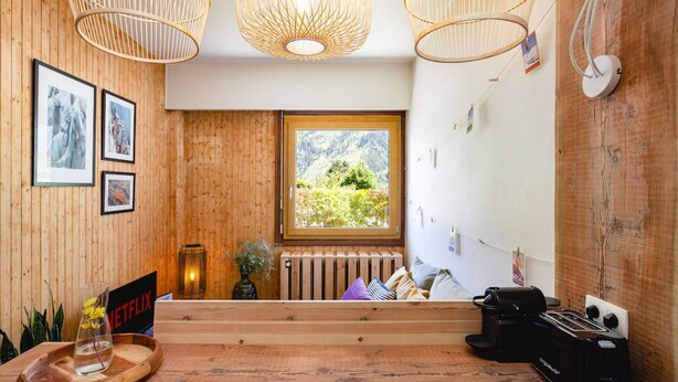 Une pièce chaleureuse avec des murs en bois, un banc en bois, un radiateur, une fenêtre donnant sur la montagne et une table avec une bouilloire et un grille-pain.