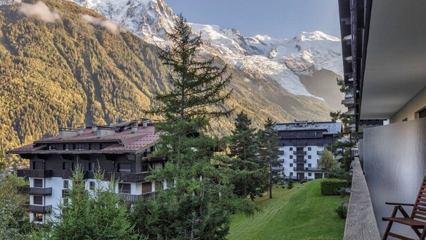 Vista de montaña con una cabaña de estilo alpino y un moderno complejo de apartamentos.