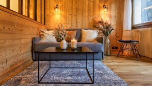 A cozy room with a wooden wall, a grey sofa, a coffee table, and a wicker chair. - Modern Apart | MtBlanc View | 5mn Slopes | Parking (Chamonix-Mont-Blanc)