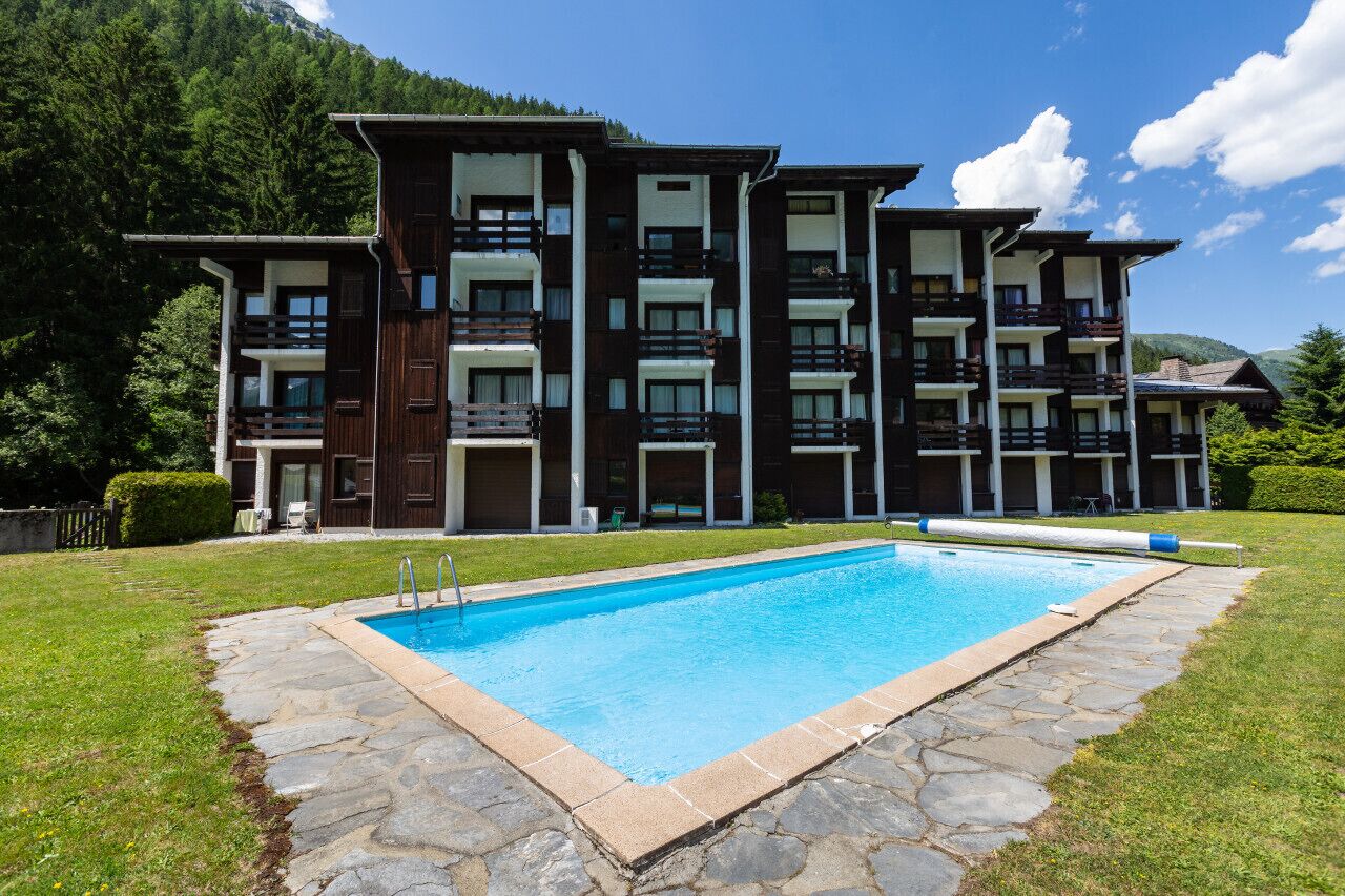 Un hôtel à plusieurs étages doté d’une piscine entourée de carreaux de pierre, le tout situé dans un cadre verdoyant luxuriant, avec des montagnes en toile de fond.