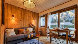 A cozy room with a wooden interior, a sofa, a coffee table, and a dining area with chairs and a table set for two. - Modern Apart | MtBlanc View | 5mn Slopes | Parking (Chamonix-Mont-Blanc)
