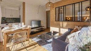 A modern living room with a wooden ceiling, a television, a dining area with a table and chairs, and a sofa. - Modern Apart | MtBlanc View | 5mn Slopes | Parking (Chamonix-Mont-Blanc)