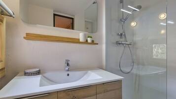 Une salle de bain moderne avec un lavabo blanc, des meubles en bois, un miroir et une douche à parois de verre.