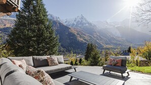 Un espace de détente extérieur moderne, comprenant un canapé et un fauteuil, une table basse en bois et une vue sur les montagnes.