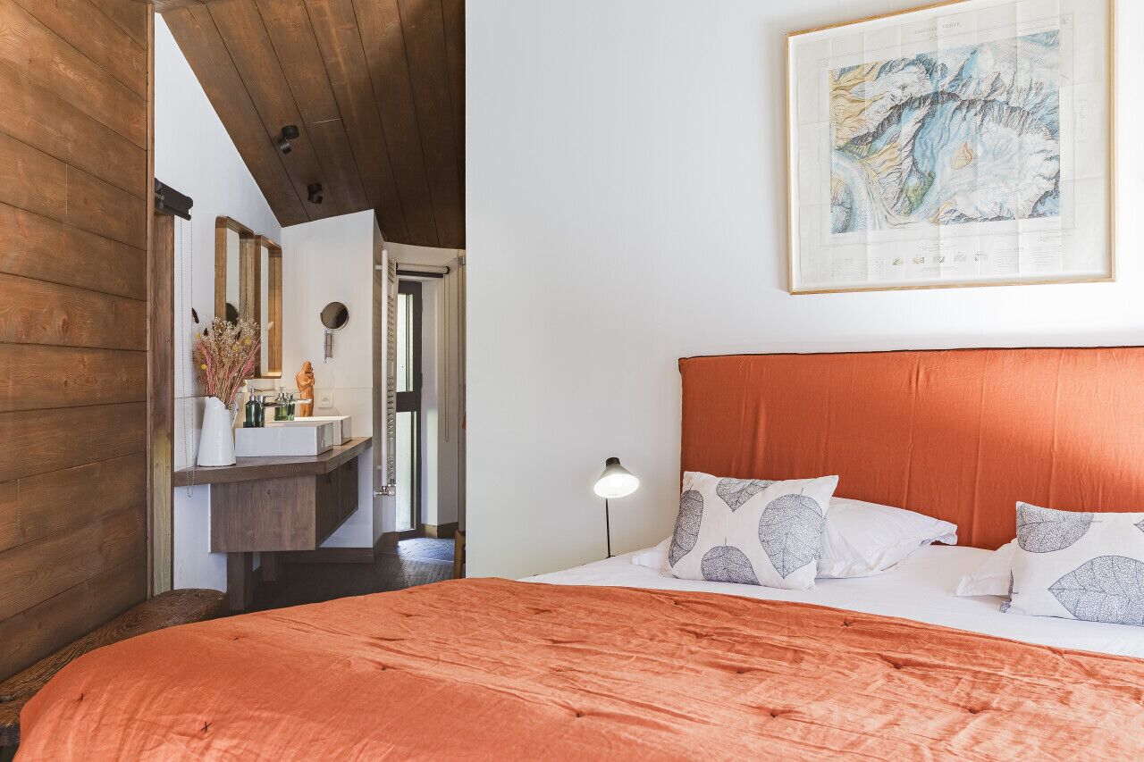 A bedroom with a wooden headboard, a large bed with patterned pillows, a nightstand with a lamp, and a framed map on the wall.