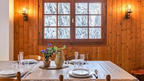 Une table à manger dressée avec des assiettes, des verres et des couverts, un vase rempli de fleurs et une fenêtre donnant sur un paysage enneigé.